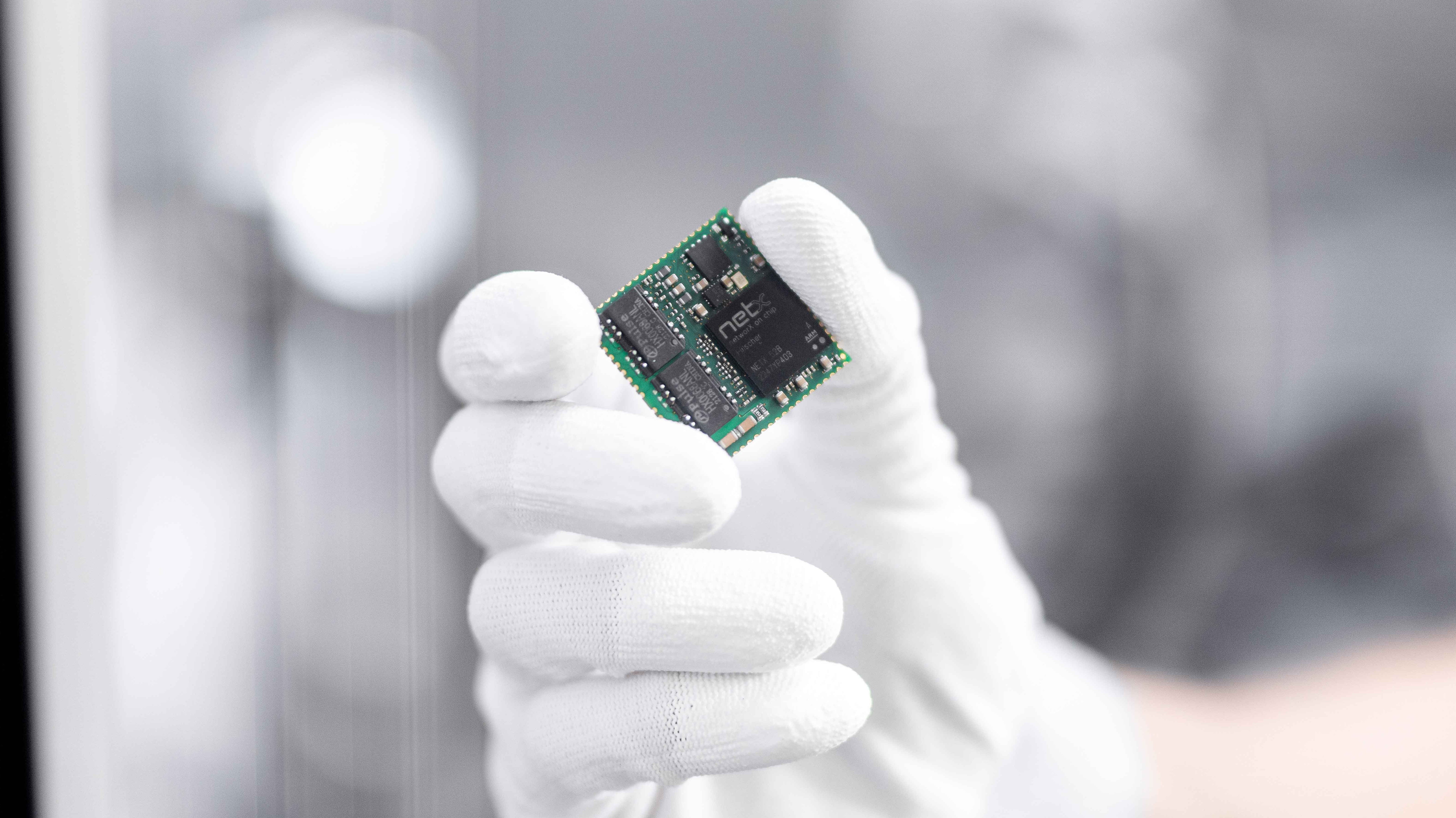 A hand in a white glove holds an embedd module from Hilscher. Mounted on the green square module is a netX 52.