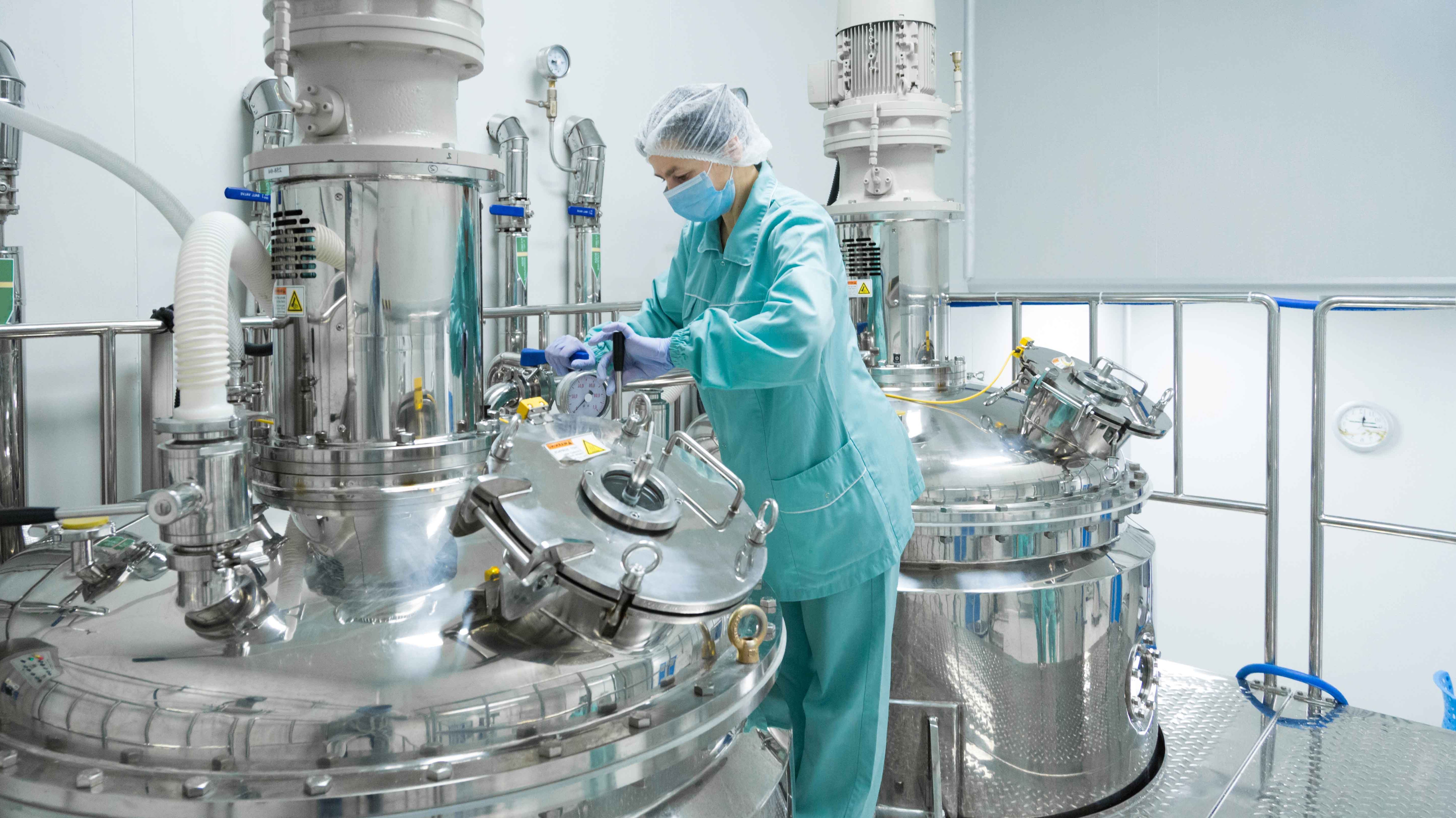 A female factory worker in pharmaceutical clothing standing beside a large fluid machinery.