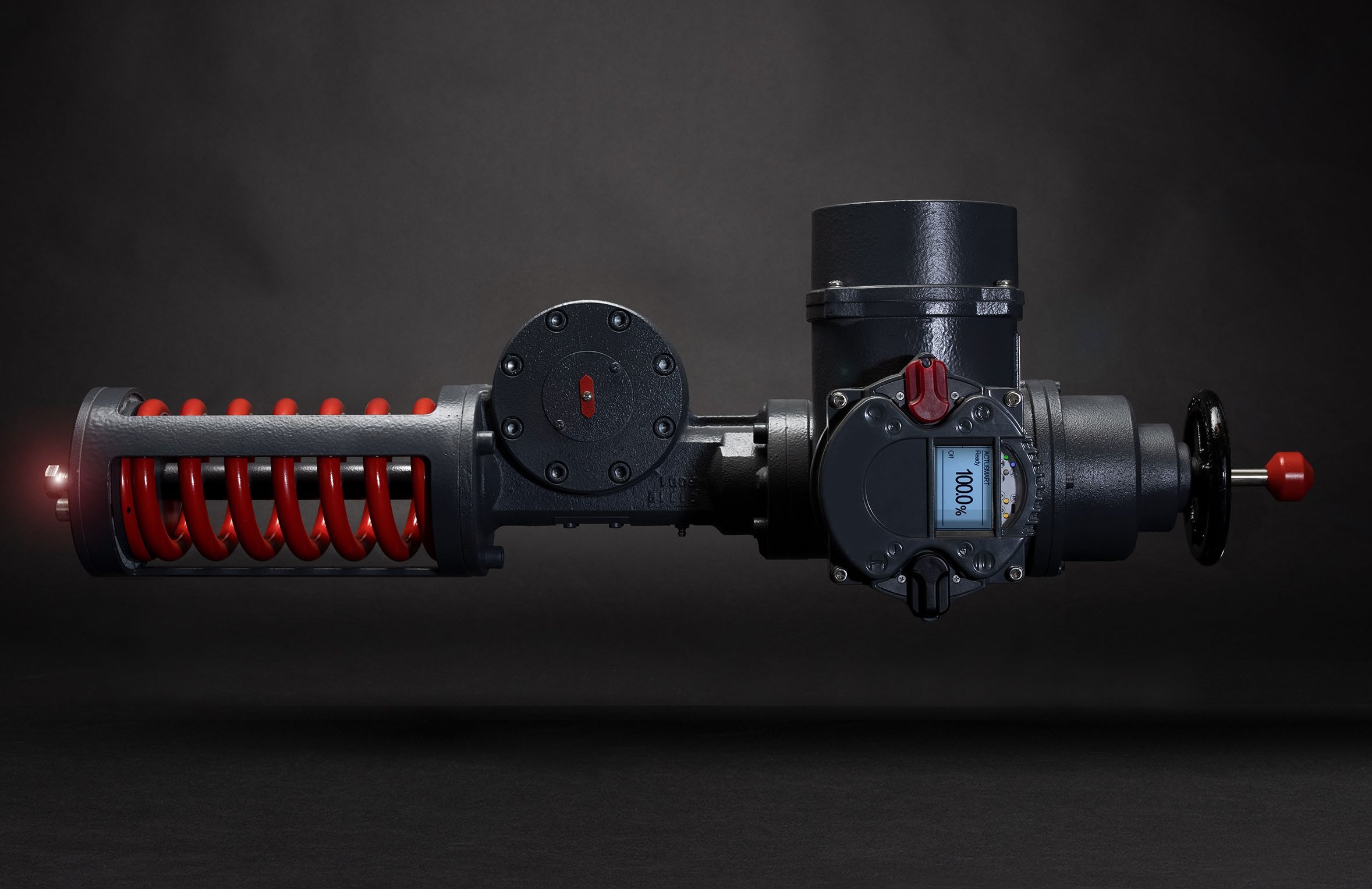 An industrial actuator by SCHIEBEL in a dark environment. On the left side of the device is a red spring. A display with "100 %" is mounted at the actuator.